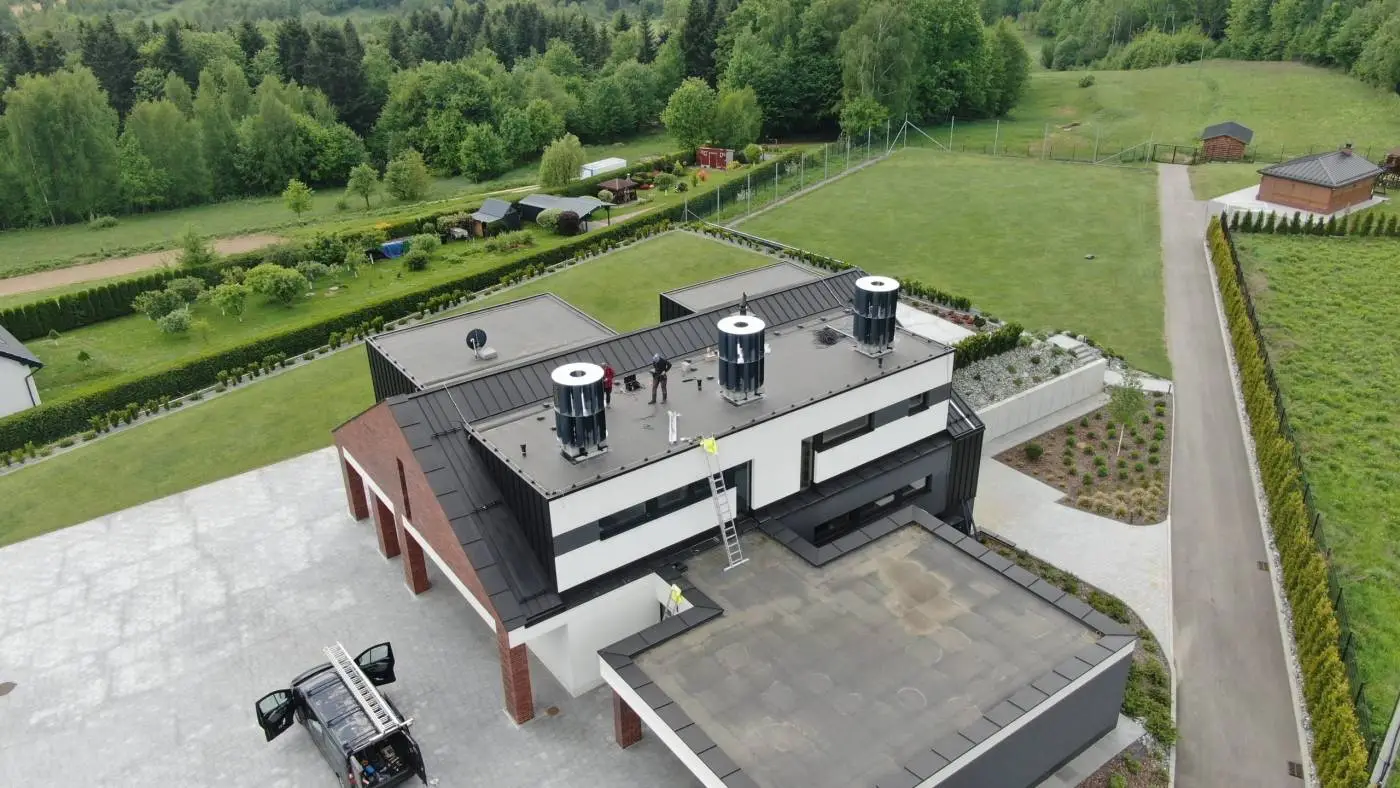 Widok z drona na nowoczesny dom z płaskim dachem i pracownikami przy turbinach