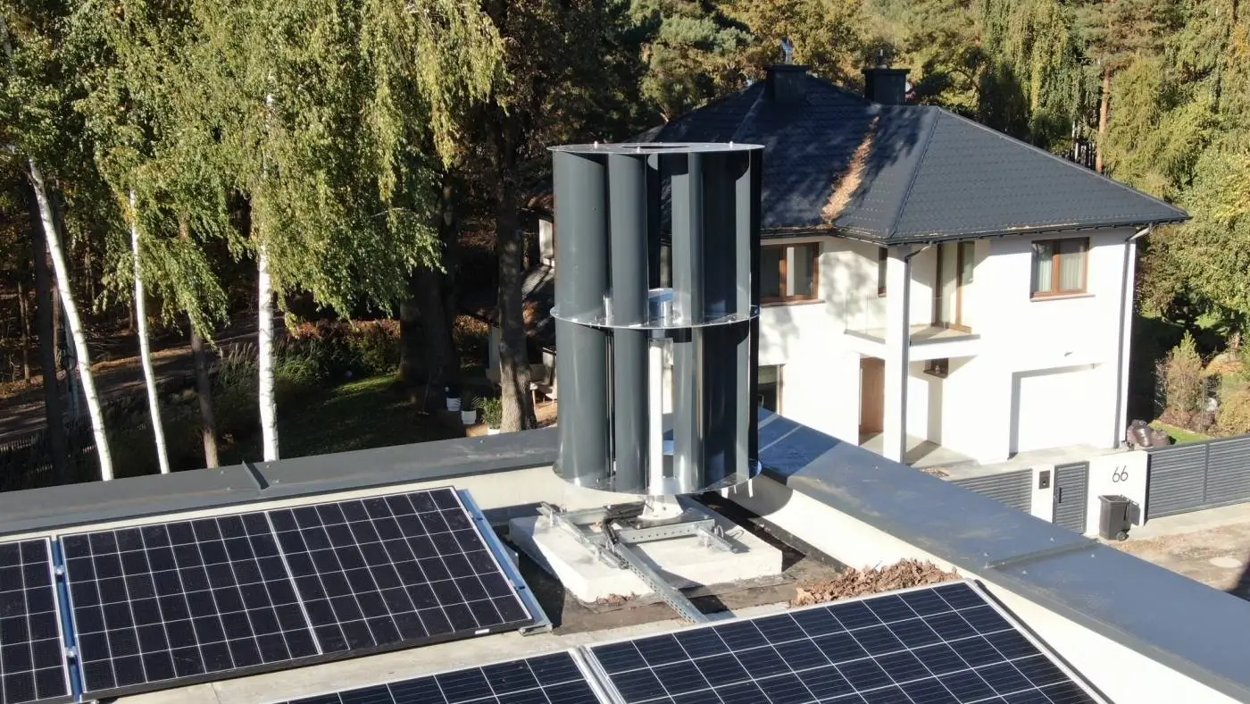 Turbina wiatrowa VAWT i panele fotowoltaiczne na dachu domu przy brzozach